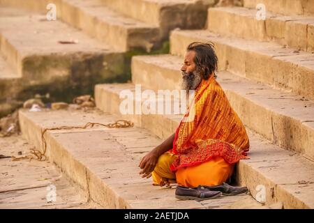 An Indian sadhu sits cross-legged in meditation on the public ghats of the ancient city of Varanasi at dawn. Stock Photo