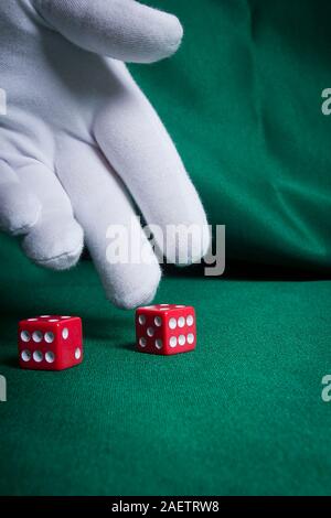 Hand in a white glove throwing red dice on the table Stock Photo