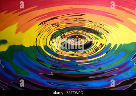 The Gay Pride Extinction Rebellion flag and logo reflected in circular waves from a water splash along with two falling droplets of water. Stock Photo