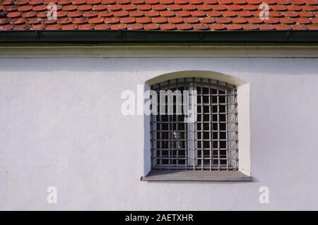 Old historic white plastered and weathered facade with a window and a grid of iron in front of red roof as background in Bavaria Stock Photo
