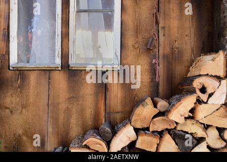 Background of an old romantic weathered wooden wall with an old window, a cord with bells in front of it and firewood Stock Photo
