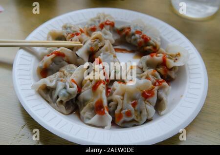 Dumplings with hot sauce and chopsticks on a styrofoam plate at a small restaurant in Chinatown, Manhattan, New York City Stock Photo