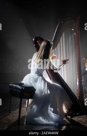 girl playing the harp on stage during a concert Stock Photo