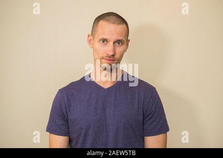 Attractive brutal bearded guy poses in blank purple t-shirt on light biege background. Stock Photo