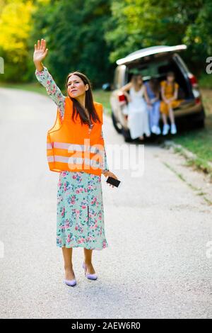 Woman in orange reflective vest is catching car having broken car, family in back Stock Photo