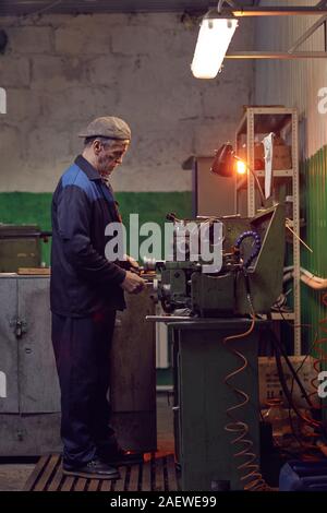 Serious mature man standing and working at the machine in the plant Stock Photo