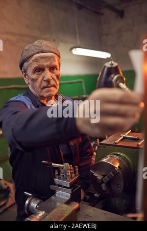 Mature worker standing and working with details on the machine in the factory Stock Photo