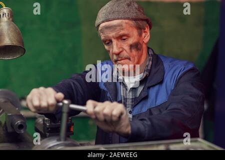 Senior manual worker standing and turning the lever of the machine in the factory Stock Photo