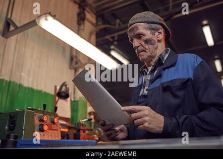 Manual worker in work wear reading the contract while sitting in the plant Stock Photo