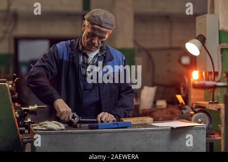 Senior manual worker repairing details at the lathe in the plant Stock Photo