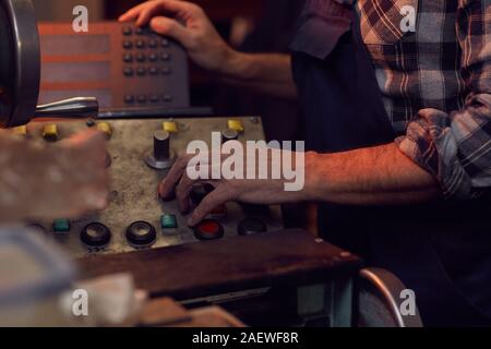 Close-up of senior manual worker standing and turning on the machine before the work in the plant Stock Photo