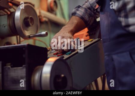 Close-up of operator in overalls controlling the work of machine using buttons in the factory Stock Photo