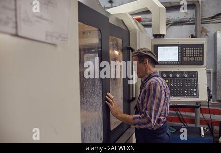 Senior engineer looking through the window and controlling the work of the lathe while standing in the plant Stock Photo