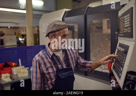 Senior operator in overalls standing in the factory and regulating the operation of the machine Stock Photo
