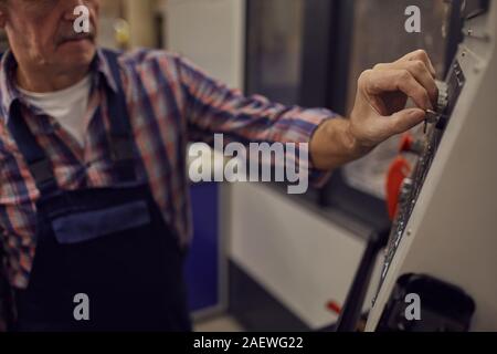 Close-up of mature engineer using computer on the machine while working in the factory Stock Photo