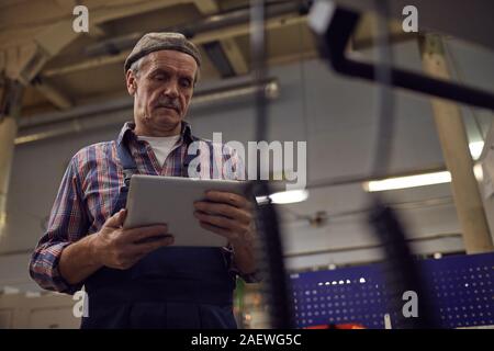 Senior operator using digital tablet and controlling the work of machine online in the factory Stock Photo