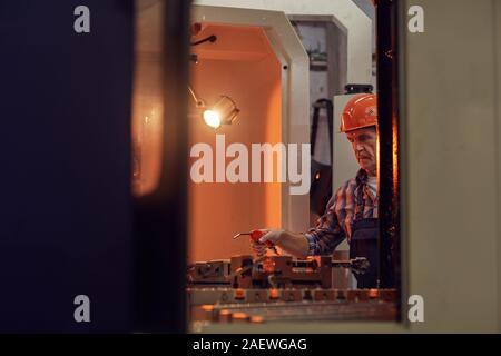 Mature electrician in work helmet working with special equipment at the lathe in the plant Stock Photo