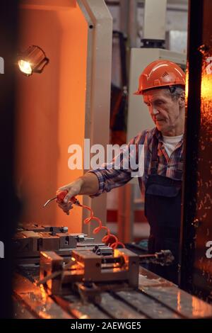 Serious mature manual worker using blowed equipment while working with metal in the factory Stock Photo