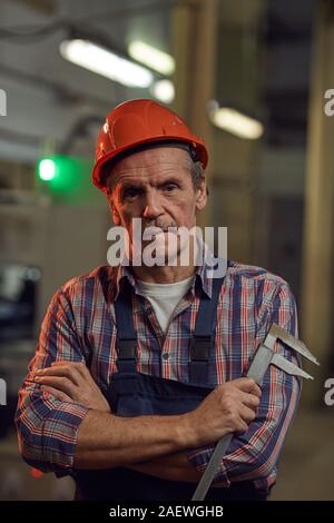 Portrait of senior foreman in work helmet looking at camera while standing with measuring work tool Stock Photo