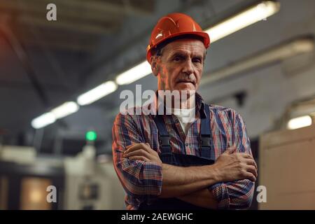 Portrait of confident senior foreman in protective work wear standing with arms crossed and looking at camera Stock Photo