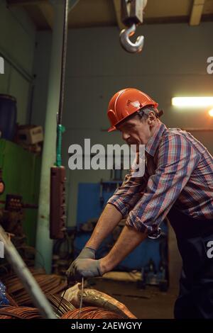 Senior mature construction worker in work helmet unpacking the metal cables before work in workshop Stock Photo