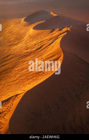 Aerial view of a large red sand dune in the Namib Desert at sunset, showing its lines, curves, shadows, and a sharp ridge on top. Sossusvlei, Namibia. Stock Photo