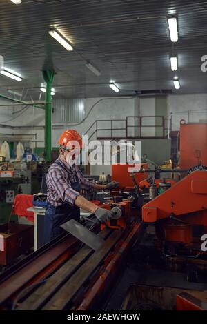 Serious mature engineer in protective eyeglasses and in work helmet controlling the machine in the factory Stock Photo