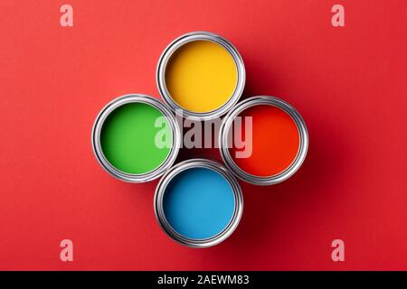 Four cans of colorful paint on red background. Top view on Green, yellow, red and blue paints. Stock Photo