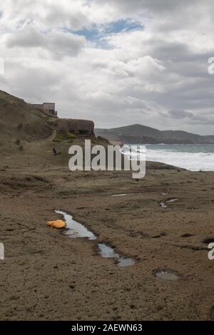 Rocky coast of the Mediterranean sea with and abandoned shelter from World War the Second. Intense rainy clouds on the spring sky. Bosa Marina, Sardin Stock Photo