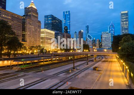 Evening twilight exterior skyline shot of downtown Chicago at night with building cityscape illuminating the dark sky view over train track rail yard Stock Photo