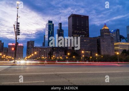 Chicago, IL - Circa 2019: Night time establishing shot of downtown Chicago skyline long exposure light trails of cars passing through busy intersectio Stock Photo