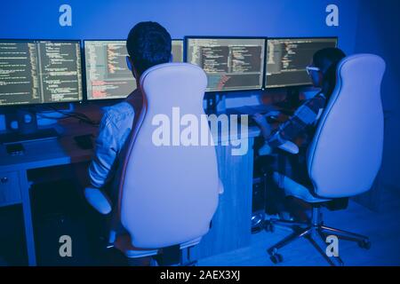 Rear behind view photo of it specialist guy lady business people night hard-working together sitting chairs many monitors testing system writing Stock Photo