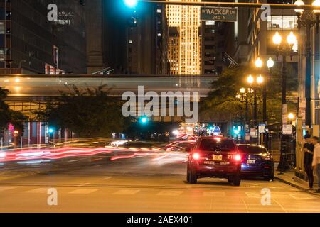 Chicago, IL - Circa 2019: Night time long exposure downtown as busy car traffic drives through intersection past pedestrian crossing people waiting at Stock Photo