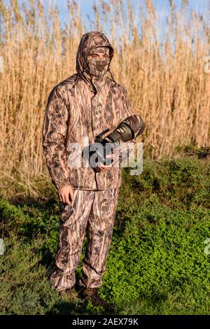 Naturalist photographer in action, with camouflage and camera, in the wilderness. Stock Photo