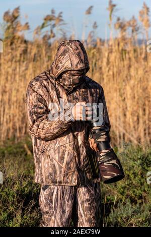 Naturalist photographer in action, with camouflage and camera, in the wilderness. Stock Photo