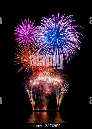 Magnificent fireworks display with happy colors on black background, reflected on water Stock Photo