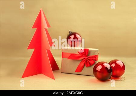 Gift box with bow and red balls with woodden Christmas tree on a natural brown background. Stock Photo