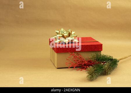 Gift box with red top and gold bow with a branch of Christmas tree on brown background Stock Photo