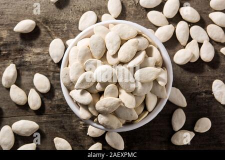 Pumpkin seeds in white bowl on wooden background. Top view Stock Photo
