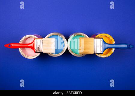 Four open cans of paint with brushes on blue background. Yellow, blue, pink, turquoise colors of paint. Top view. Stock Photo