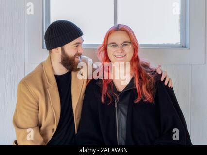 Hip Young Millennial Caucasian Couple Sitting on an Indoor Bench with Natural White Wood Background Dressed in Warm Winter Clothes Stock Photo