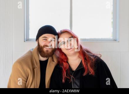 Hip Young Millennial Caucasian Couple Sitting on an Indoor Bench with Natural White Wood Background Dressed in Warm Winter Clothes Stock Photo