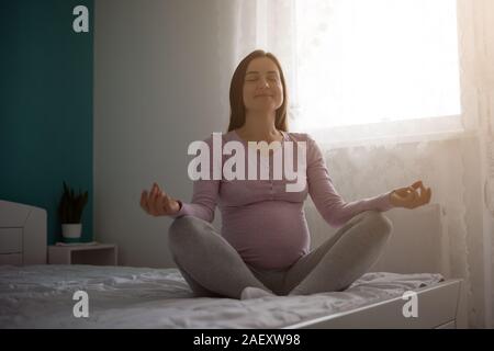 Happy pregnant woman meditating at home. Stock Photo