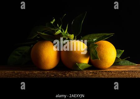 Three oranges with leaves on a wooden table on a dark background Stock Photo