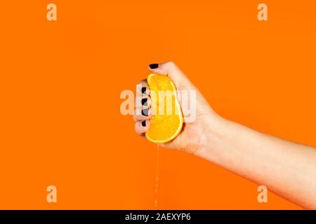 Woman squeezing a half orange on a an orange background Stock Photo