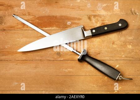 Steel sharpener and a kitchen knife on a rustic wooden table in a top view Stock Photo