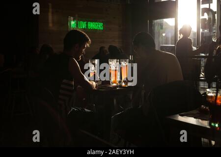 A couple pf guys is seen drinking beer in a Spanish burger place at sunset. Stock Photo