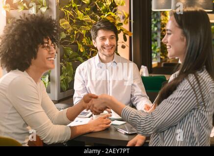 Deal. Happy young people handshaking in cafe after successful business meeting Stock Photo