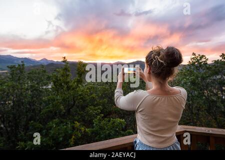 Young girl woman taking picture with phone of view at Aspen, Colorado rocky mountains colorful sunset in background Stock Photo