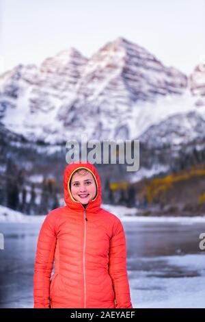 Maroon Bells sunrise with happy woman looking at camera in Aspen, Colorado rocky mountain and autumn yellow foliage view and winter snow frozen lake Stock Photo